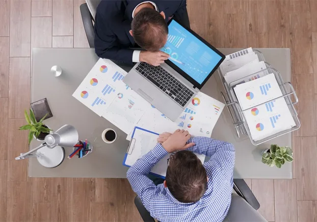 two employees sitting across a desk reviewing graphs.webp